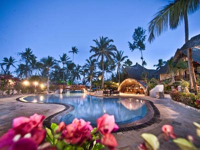 Abendliche Poollandschaft in tropischem Resort mit Palmen und Blumen im Vordergrund.