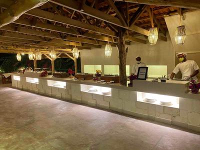 Modern beleuchteter Buffetbereich mit verschiedenen Essenstationen und einem Koch in einer offenen Küche.