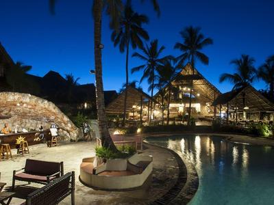 Abendaufnahme eines tropischen Resorts mit beleuchtetem Pool und Palmen.