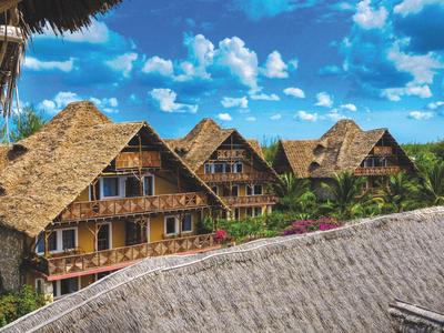 Cottage tradizionali con tetto di paglia sotto un cielo azzurro con nuvole bianche.