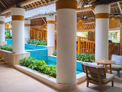 Überdachter Bereich mit Säulen, Pool und Sitzgelegenheiten in einem tropischen Hotel.