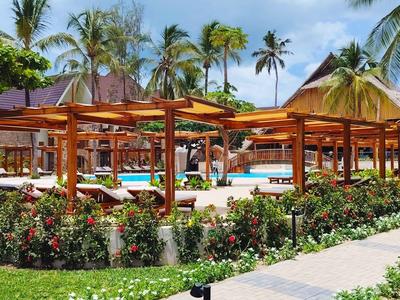 Hölzerne Pergolen und Palmen umgeben einen sonnigen Poolbereich in einem tropischen Resort.