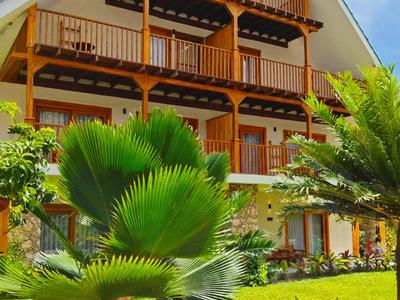 Dreistöckiges Hotel mit großen Balkonen und tropischem Garten bei sonnigem Himmel.