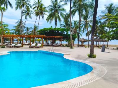 Großer Pool mit klar blauem Wasser, umgeben von Palmen und Pavillons am Strand.