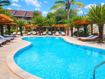 Hotelpool mit Liegestühlen und grüner Umrahmung unter blauem Himmel.