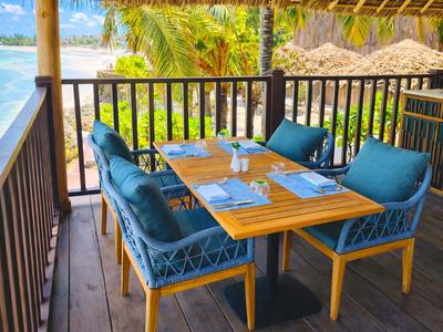 Essbereich im Freien mit blau gepolsterten Stühlen und Blick auf Palmen und Meer.