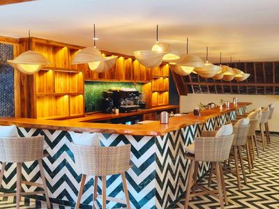 Moderner Barbereich mit buntem Zickzack-Muster, Holzelementen und vielen Hockern.