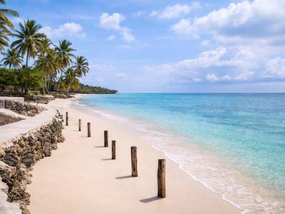 Ein ruhiger Sandstrand mit klar türkisfarbenem Wasser und Palmen im Hintergrund