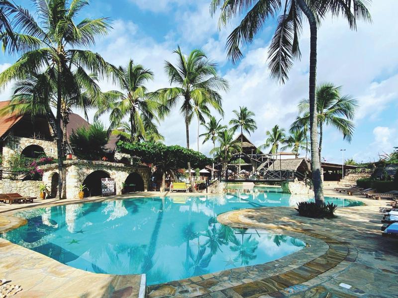 Runder Pool mit Palmen und Steinterrasse in tropischem Resort unter blauem Himmel.