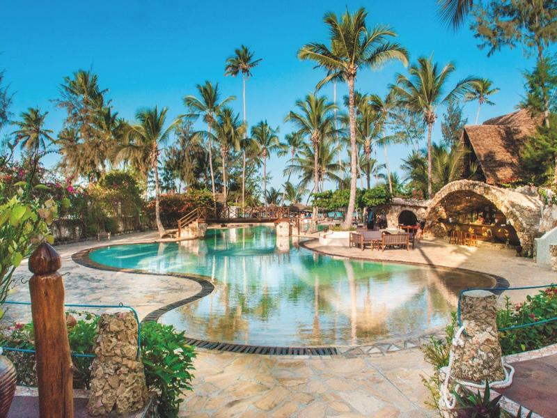 Luxuriöser Außenpool umgeben von Palmen und Liegestühlen in einer tropischen Hotelanlage.