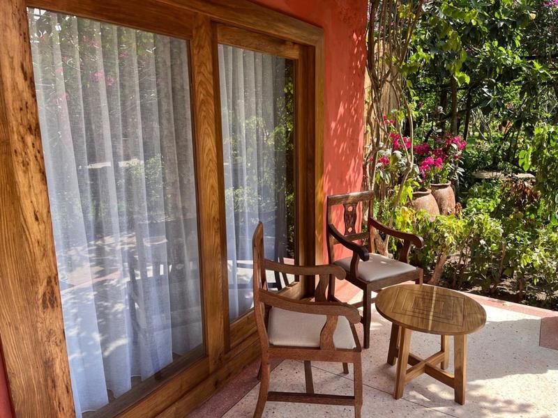 Veranda mit zwei Holzstühlen, einem kleinen runden Holztisch und weißen Vorhängen an Glastüren.