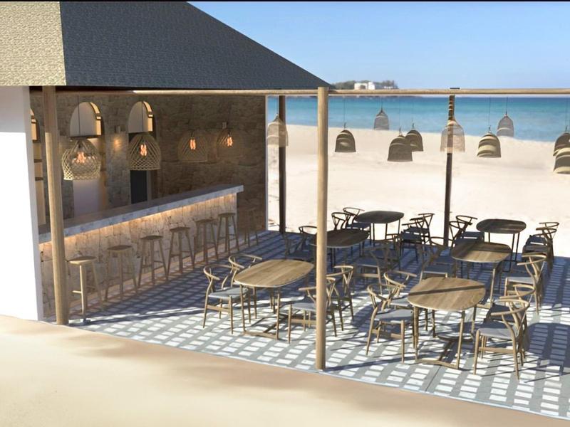 Strandbar mit Holzstühlen, runden Tischen, Hängelampen und Blick aufs blaue Meer.