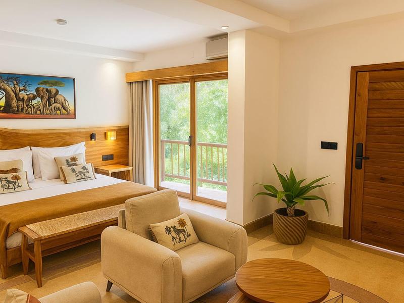 Helles Hotelzimmer mit Doppelbett, Sesseln, Pflanzen und großem Fenster mit Blick ins Grüne.