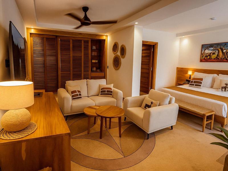 Gemütliches Hotelzimmer mit Doppelbett, Sitzecke, warmen Holzmöbeln und Deckenventilator.