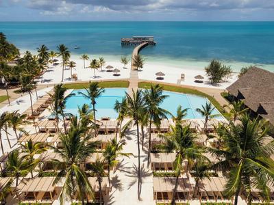 Vista di un resort con piscina, palme e molo su sabbia bianca verso il mare blu.