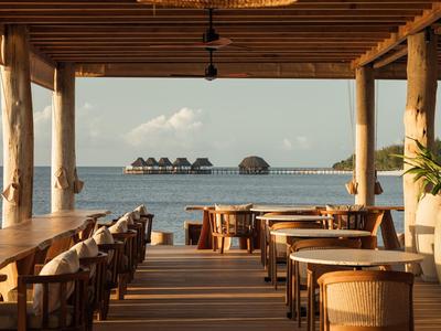 Otwarta jadalnia z drewnianymi meblami z widokiem na morze i wille nad wodą.