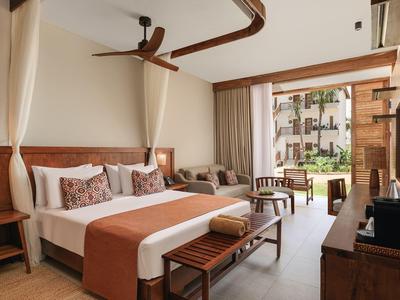 Camera d'hotel moderna con letto matrimoniale, area salotto e vista sul giardino.