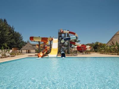 Grande piscina all'aperto con scivoli d'acqua e lettini sotto un cielo limpido.