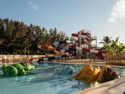 Parco acquatico con piscine, scivoli d'acqua e scivoli circondati da palme e vegetazione.