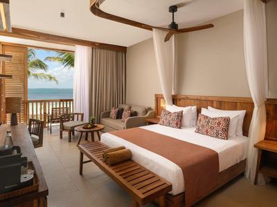 Světý hotelový pokoj s manželskou postelí, balkonem a výhledem na moře za denního světla.