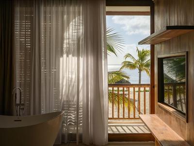 Nowoczesna łazienka z wolnostojącą wanną i widokiem na balkon z palmami i morzem.