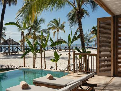 Dwa leżaki na tarasie z basenem, palmami i widokiem na morze w tle.