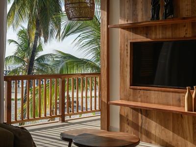 Przytulny balkon hotelowy z drewnianymi meblami i widokiem na palmy i plażę.