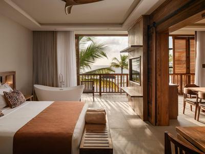 Elegancki pokój hotelowy z łóżkiem podwójnym i widokiem na morze przez otwarte drzwi balkonowe.