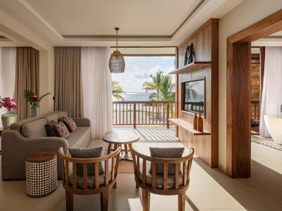 Jasny pokój hotelowy z miejscem do siedzenia, drewnianymi meblami i widokiem na morze z palmą.