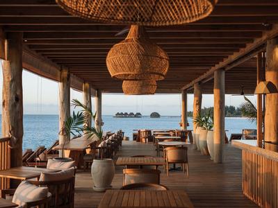 Otevřená dřevěná terasa s jídelním koutem a výhledem na moře za západu slunce.