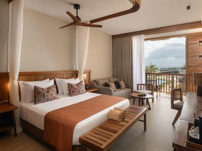 Camera d'albergo con letto matrimoniale, divano, balcone e vista mare alla luce del giorno.