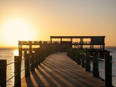 Un molo con ringhiere conduce a una piattaforma panoramica al tramonto sul mare.