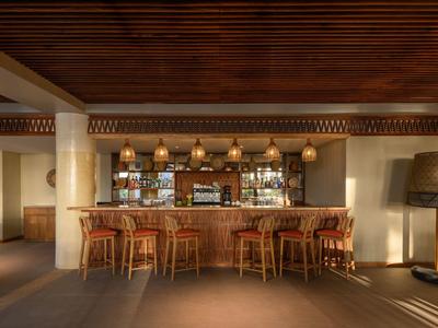 Bar dell'hotel con bancone in legno, sedie in vimini e illuminazione calda, circondato da un interno moderno.