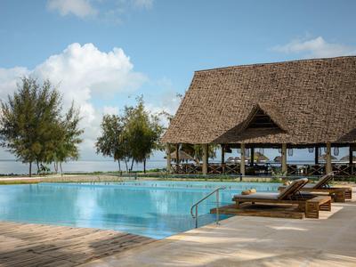 Area piscina con lettini e padiglione coperto vicino all'acqua sotto un cielo blu.