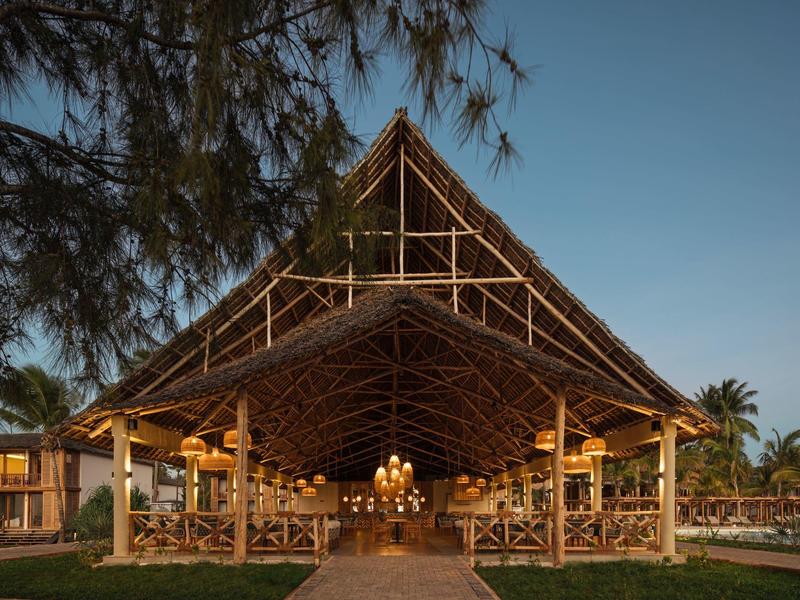 Padiglione aperto con tetto in legno e illuminazione in un ambiente tropicale di un hotel al tramonto.