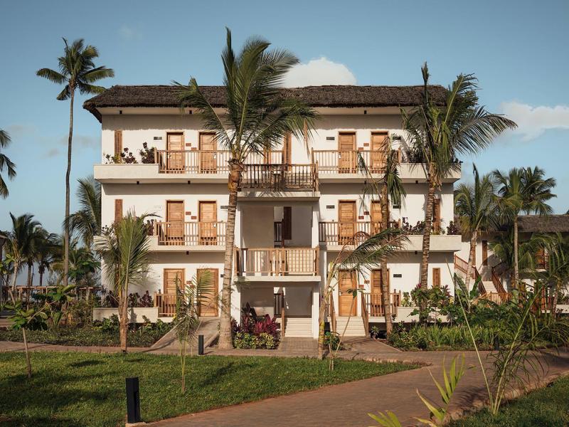 Edificio dell'hotel di tre piani con balconi, circondato da palme e giardini.