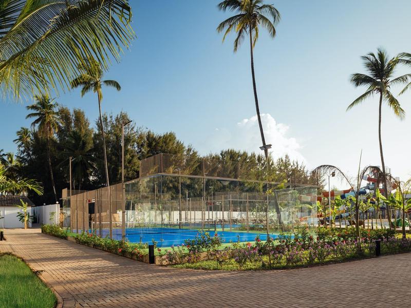 Area piscina con rete da pallavolo circondata da palme e sentieri in un hotel tropicale.