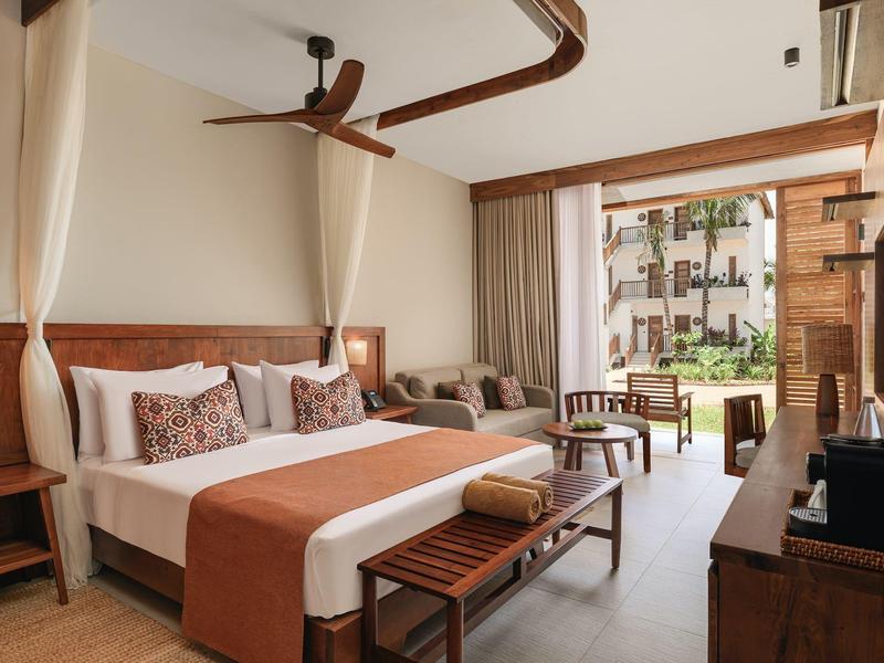 Camera d'hotel moderna con letto matrimoniale, area salotto e vista sul giardino.