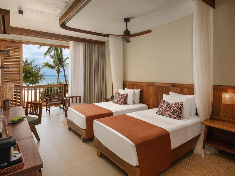 Camera d'hotel luminosa con due letti singoli, mobili in legno e vista mare dal balcone.