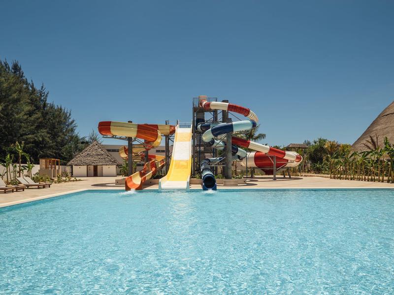 Grande piscina all'aperto con scivoli d'acqua e lettini sotto un cielo limpido.