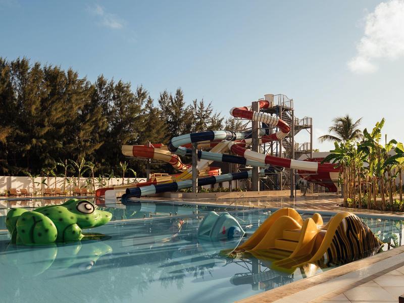 Parco acquatico con piscine, scivoli d'acqua e scivoli circondati da palme e vegetazione.