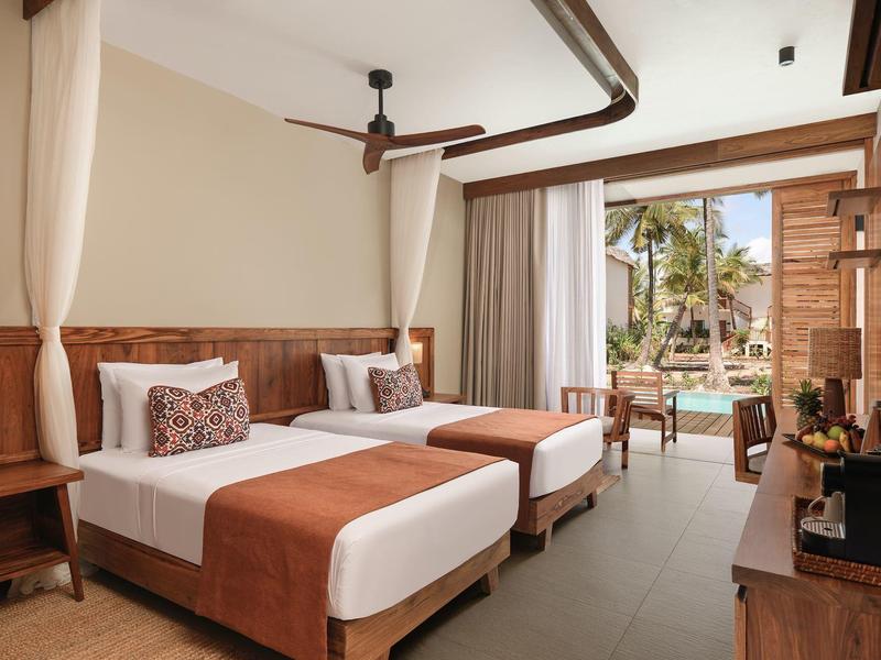 Camera d'hotel con due letti, pannelli in legno scuro, ventilatore a soffitto e vista sulla piscina.
