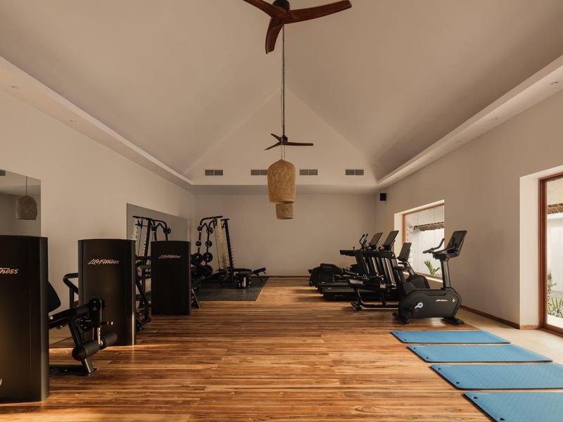 Palestra moderna con pavimento in legno, attrezzature e tappetini per yoga in una stanza luminosa.