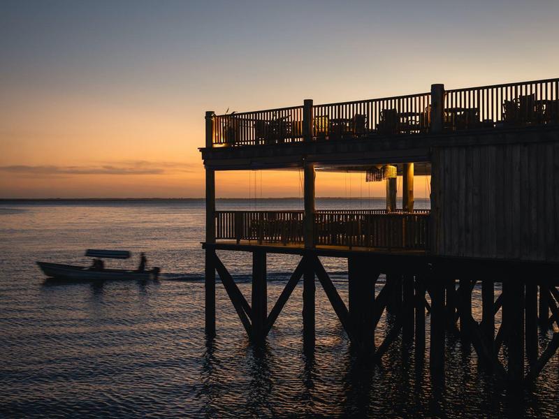 Tramonto sul mare con un pontile e una piccola barca in acqua.
