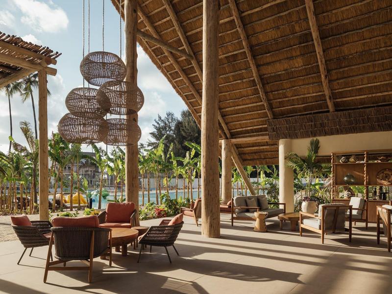 Area lounge aperta dell'hotel con soffitti in legno, mobili moderni e piante tropicali.