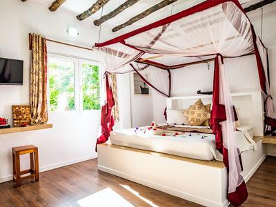 Helles Schlafzimmer mit Himmelbett, weißen Wänden, Holzbalken und großem Fenster mit Gardinen.