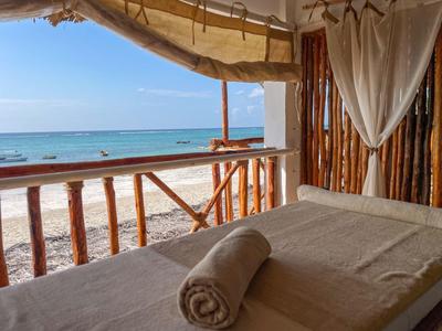 Offene Terrasse mit Holzgeländer, Bett mit beiger Decke und Rolle, Blick auf Strand und Meer.