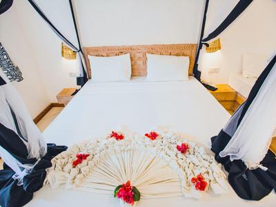 Weißes Bett mit zwei Kissen, Holz-Kopfteil, Stoffdekoration und roten Blumen als Akzent.