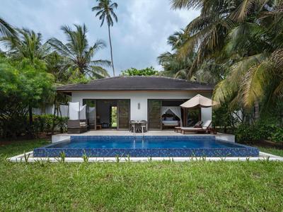 Ein modernes Haus mit Glasschiebetüren, umgeben von Palmen und einem klaren blauen Pool vor grünem Rasen.