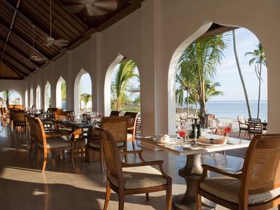 Open restaurant with wooden furniture and views of palm trees and the sea.